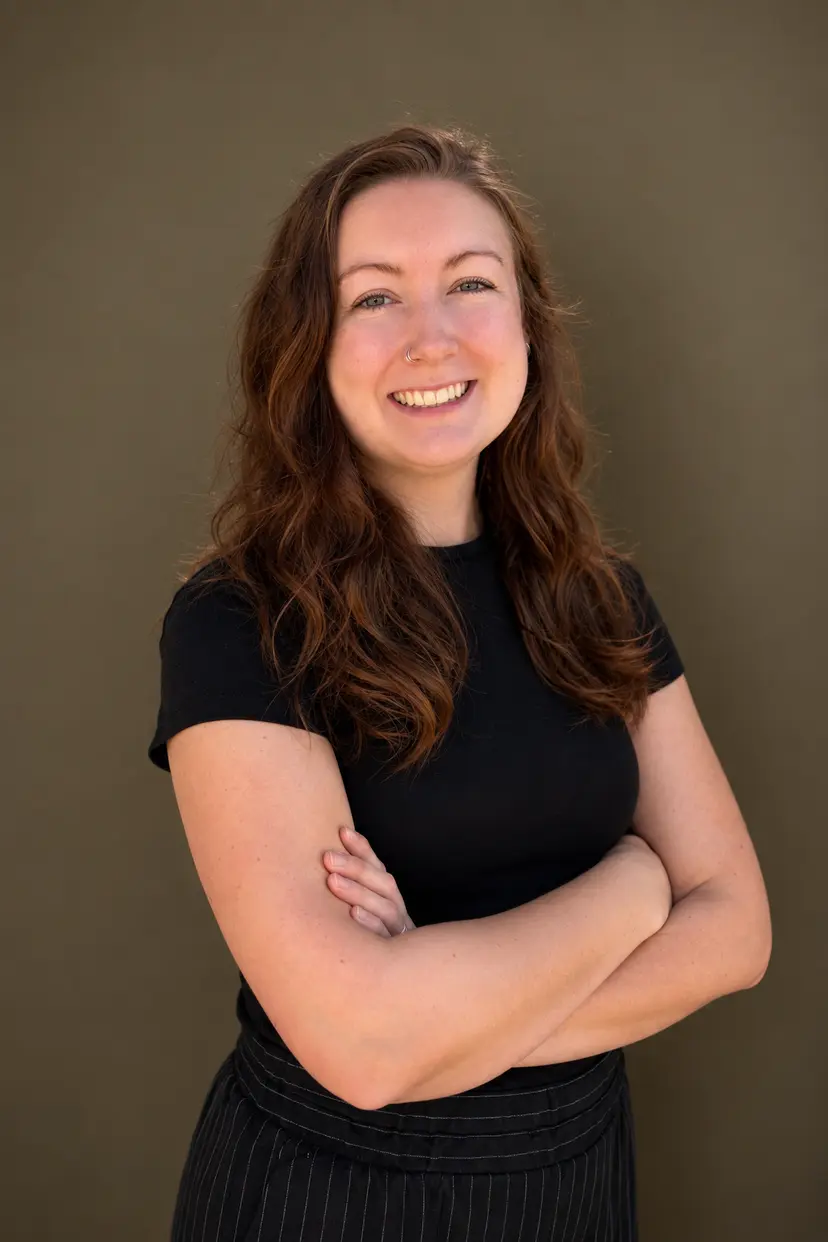 Caitlin smiling with folded arms in a black shirt against a neutral studio backdrop
