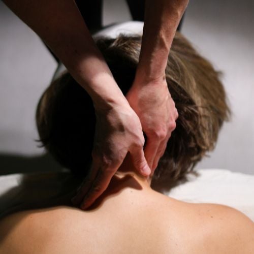 Hands performing massage on person's upper back and shoulder area.