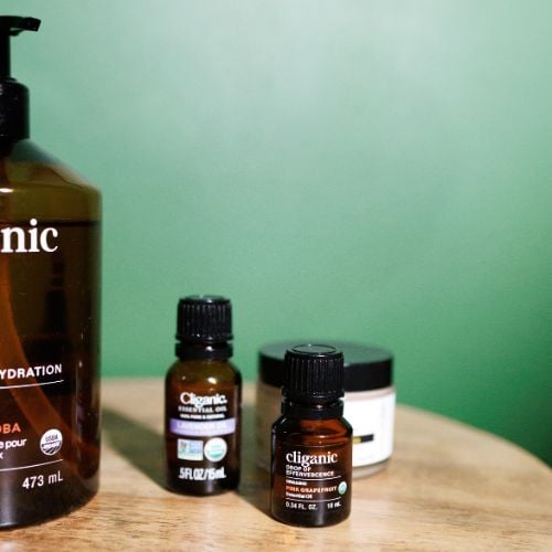 Skincare products on wooden surface against mint green background, including pump bottle and dark glass jars