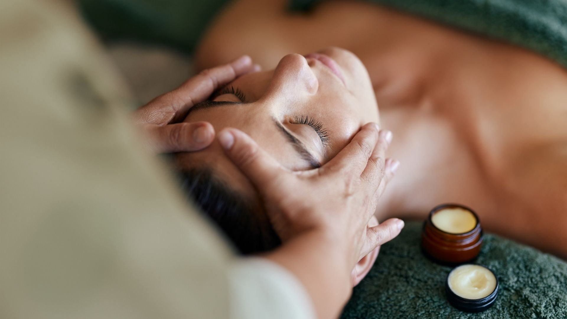 Spa facial massage treatment with closed eyes, relaxation, and skincare products nearby.