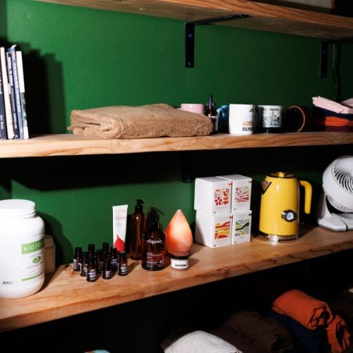 Wooden shelves against bright green wall displaying towels, bottles, mugs, and household items