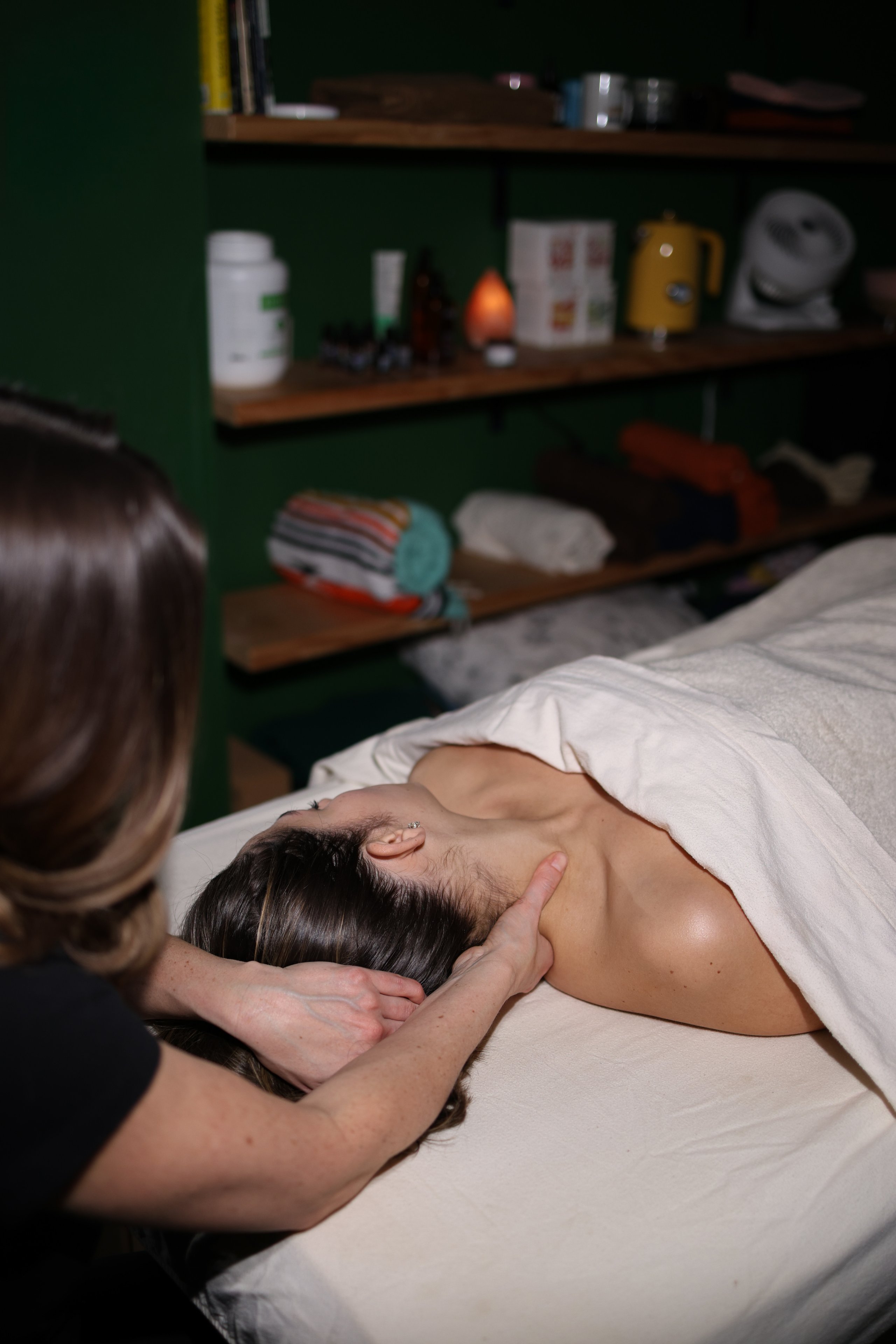 Massage therapist treating man lying on bed in wellness studio with green walls
