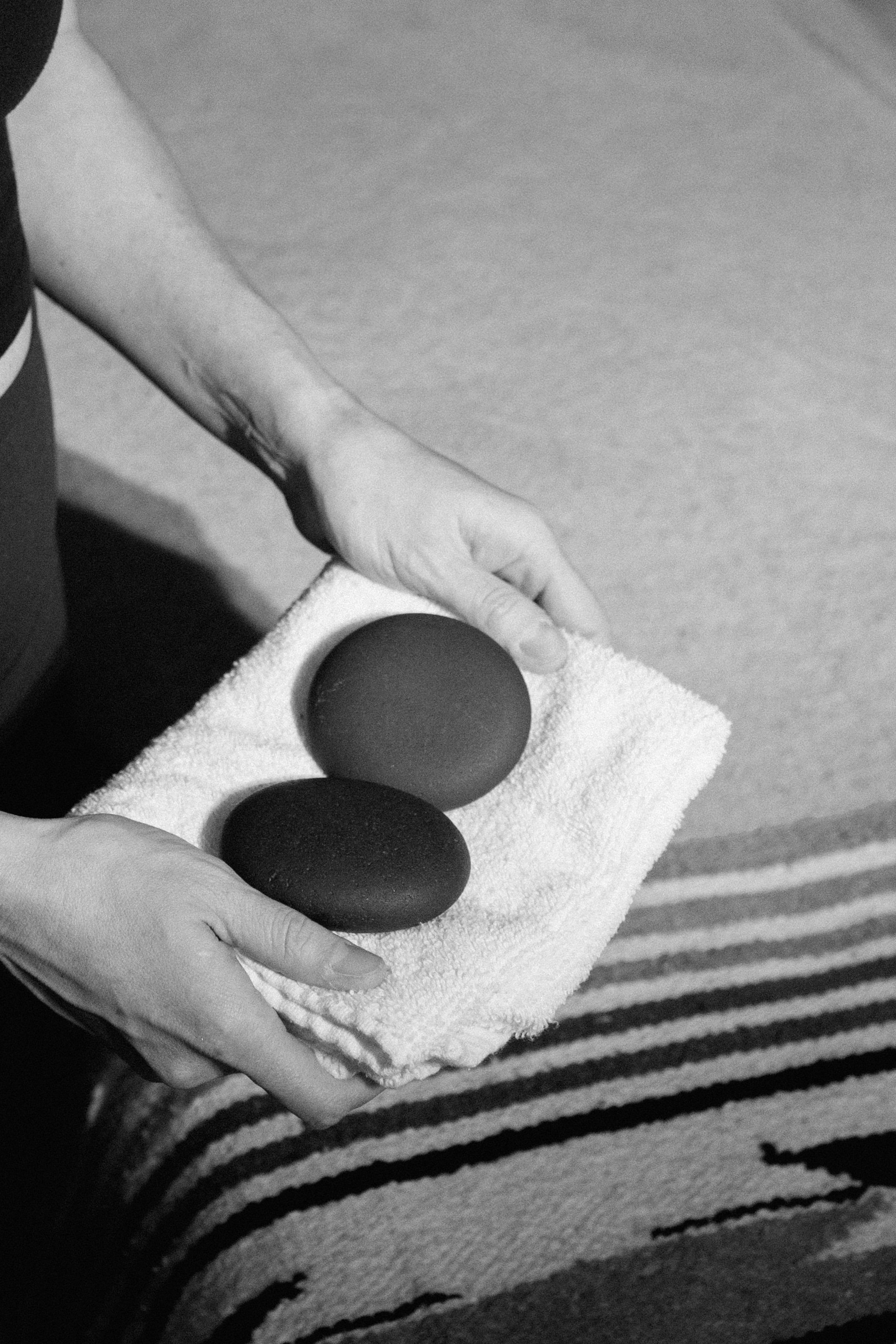 Person holding two black massage stones on a white towel, black and white photo