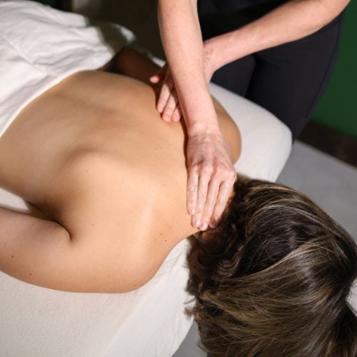 Massage therapist performing back massage on female client lying on table.
