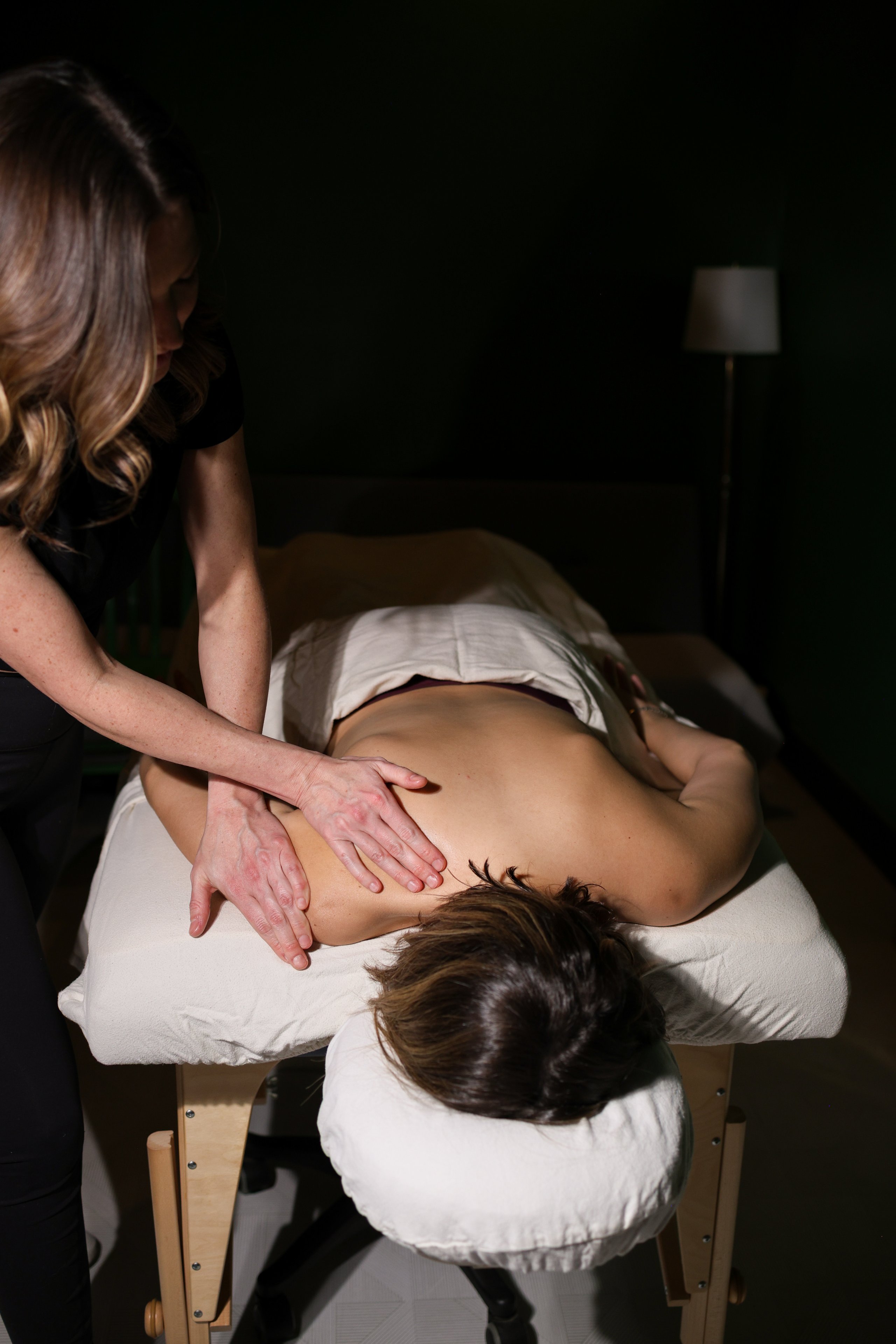Massage therapist performing back massage on client lying on table in dim lighting