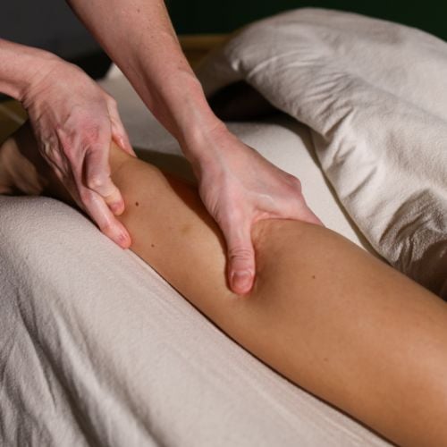 Massage therapist's hands performing leg massage on client lying on bed