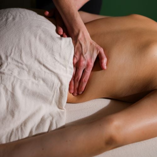 Massage therapist providing therapeutic leg massage to a client on white sheet