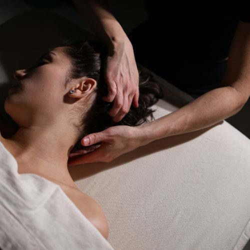 Therapist performing neck and shoulder massage on relaxed client in white shirt